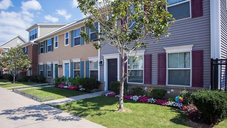 Tan and gray townhomes with shutters, individual entries, and resident plantings